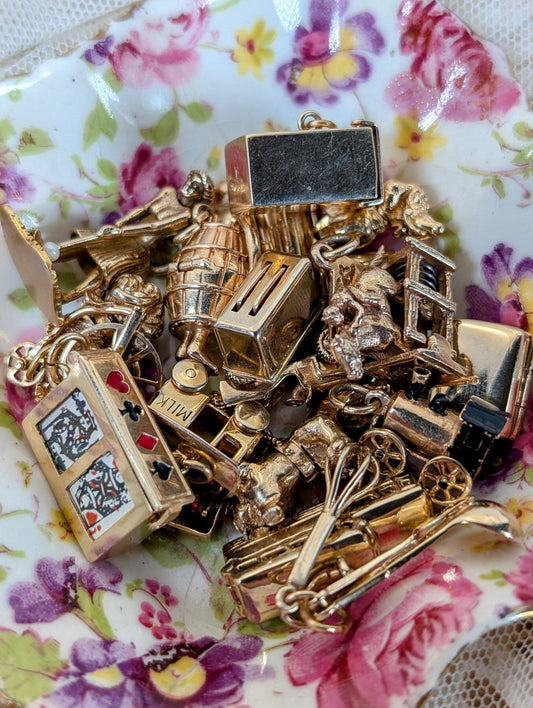 A pile of 14k gold mechanical charms on a vintage floral China dish