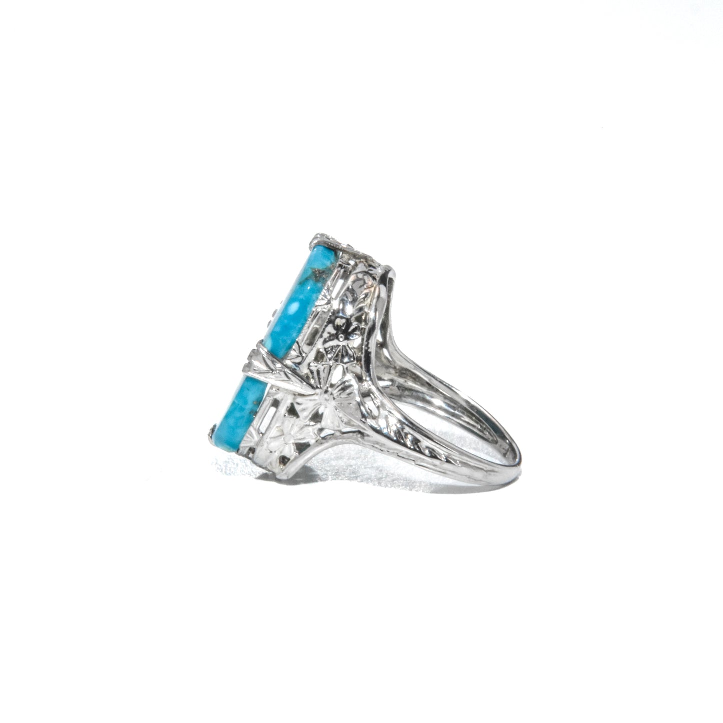 An Art Deco style 14K white gold ring with a large turquoise stone and intricate filigree design.