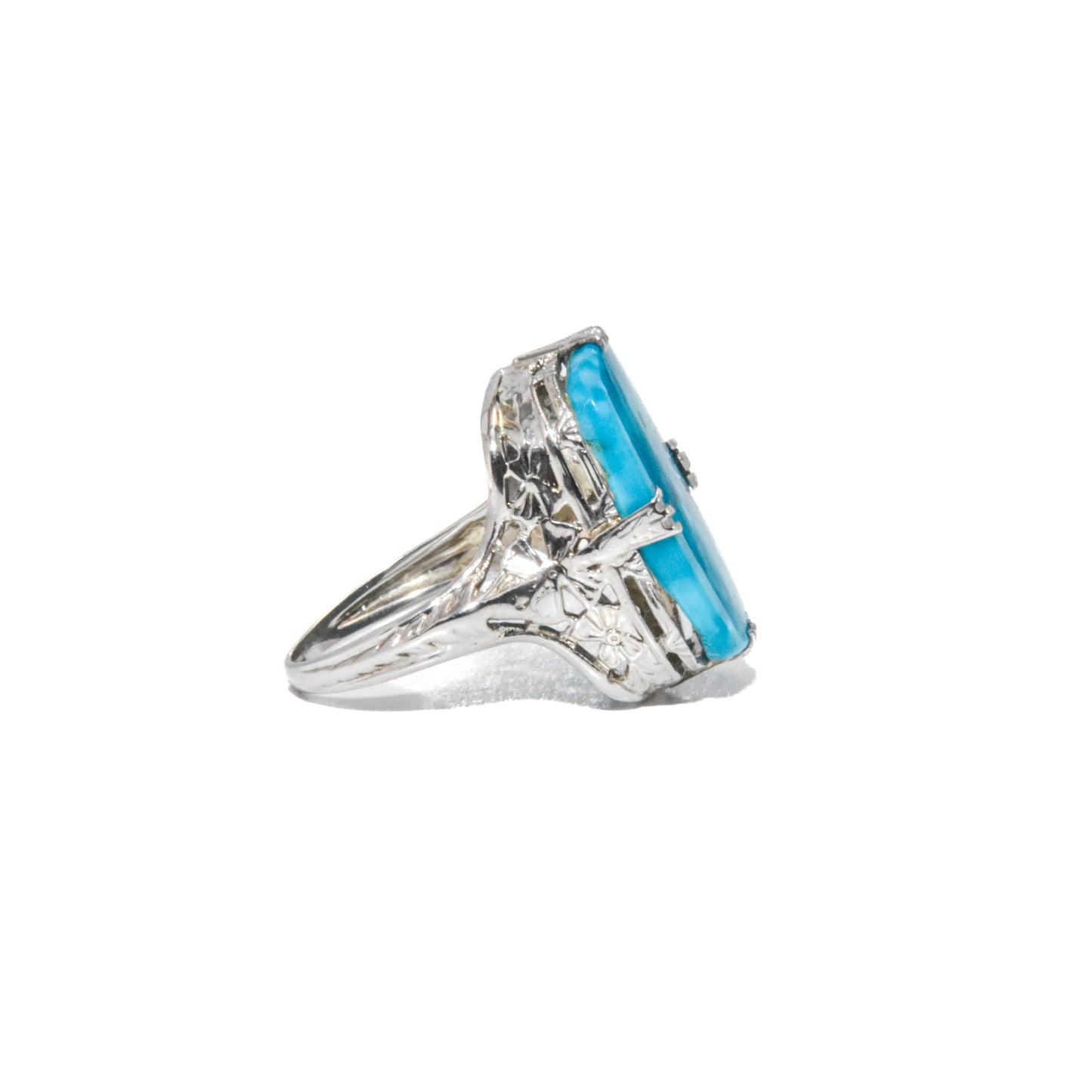 An Art Deco style 14K white gold ring with a large turquoise stone and intricate filigree design.