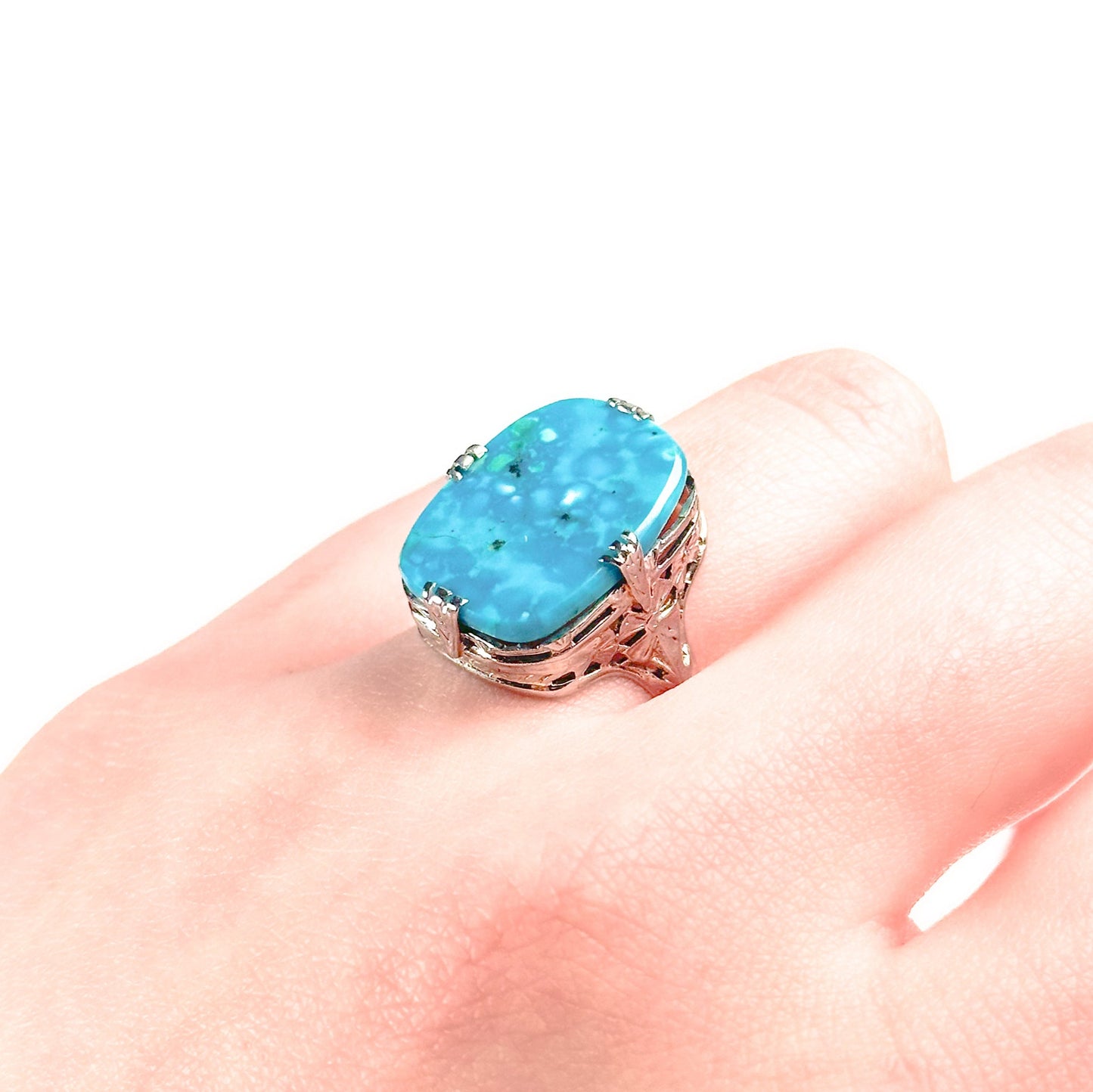 An Art Deco style 14K white gold ring on a finger with a large turquoise stone and intricate filigree design.