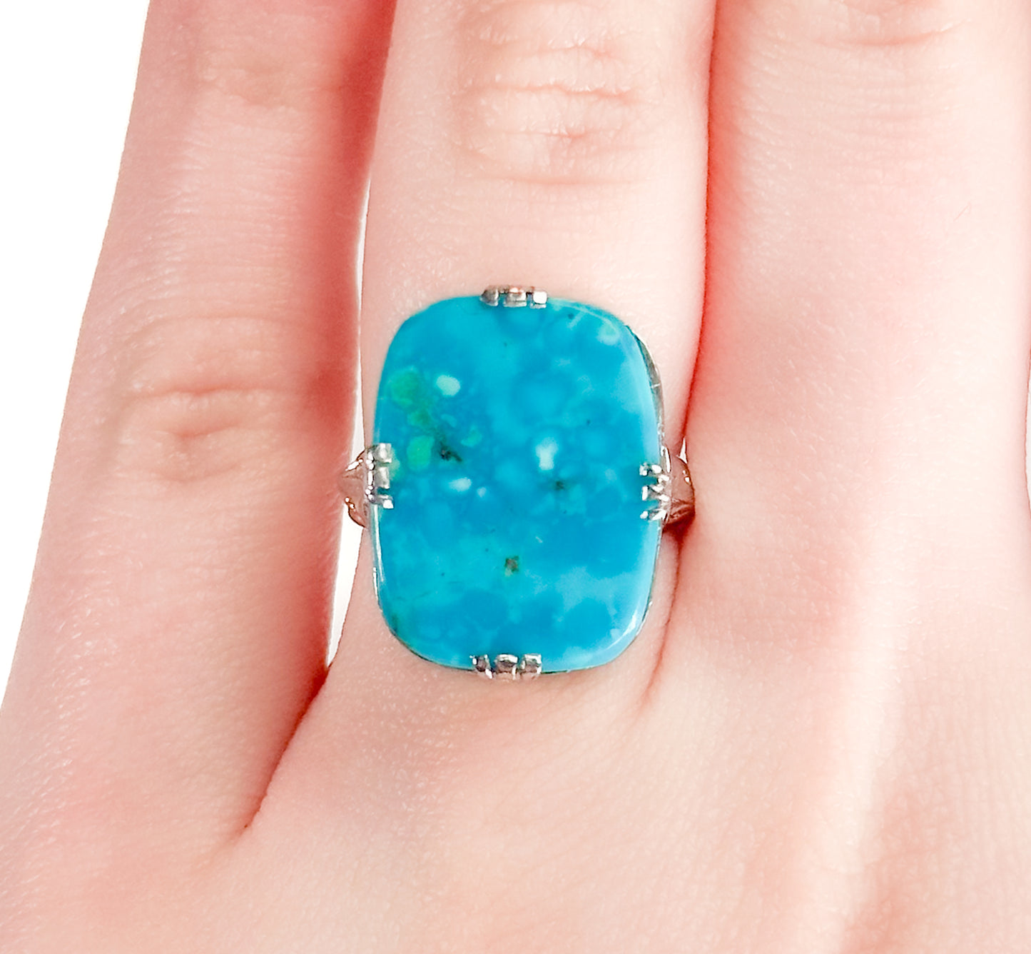 An Art Deco style 14K white gold ring on a hand with a large turquoise stone and intricate filigree design.