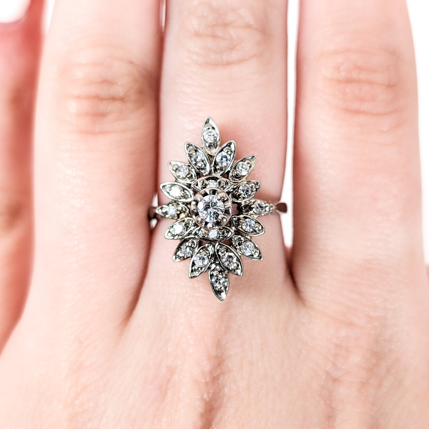 Luminous 14K white gold ring , the design features a brilliant round center diamond surrounded by an intricate halo of marquise-shaped with round diamond accents on a finger on a hand