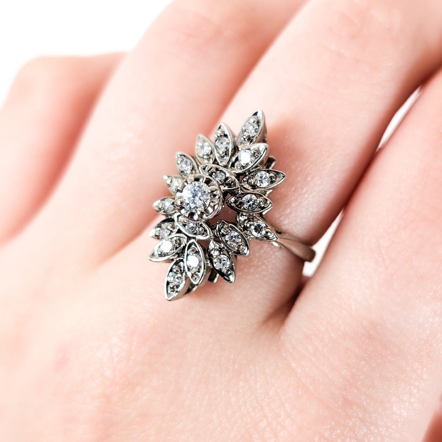 Luminous 14K white gold ring , the design features a brilliant round center diamond surrounded by an intricate halo of marquise-shaped with round diamond accents on a finger on a finger