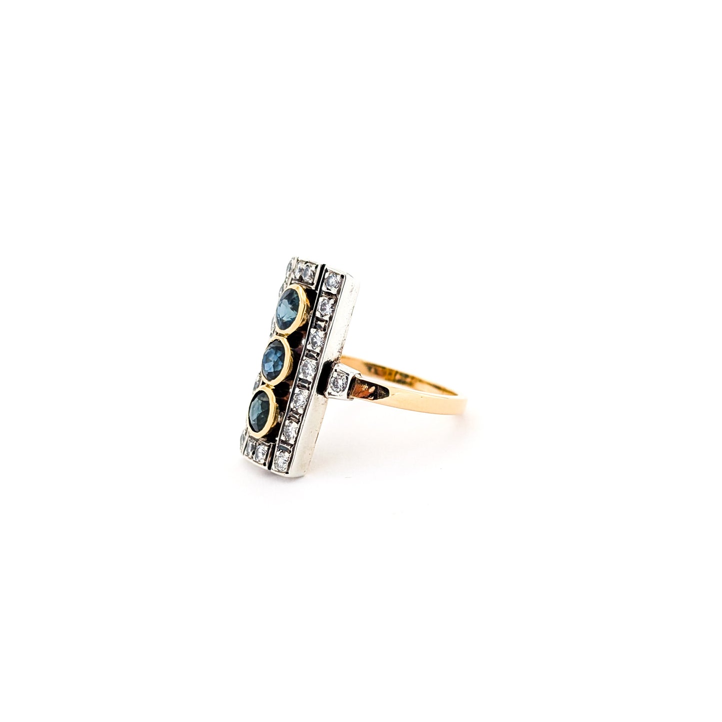 Elegant dinner ring, crafted in Italy, blends the warmth of 18K yellow gold with the cool brilliance of silver. The ring features a striking rectangular design with three deep blue sapphires, their rich color evoking the Mediterranean night sky against a white background.
