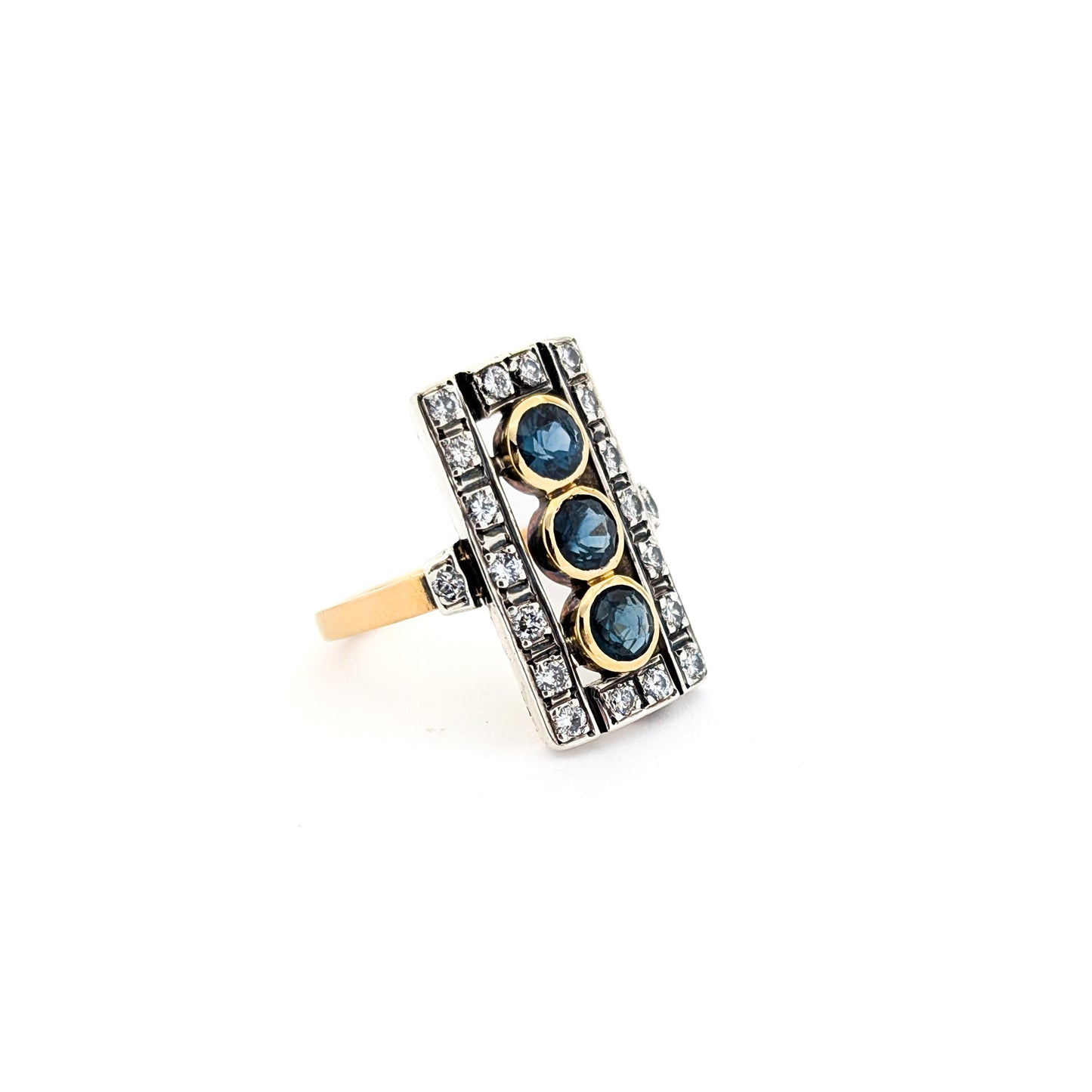 Elegant dinner ring, crafted in Italy, blends the warmth of 18K yellow gold with the cool brilliance of silver. The ring features a striking rectangular design with three deep blue sapphires, their rich color evoking the Mediterranean night sky against a white background.