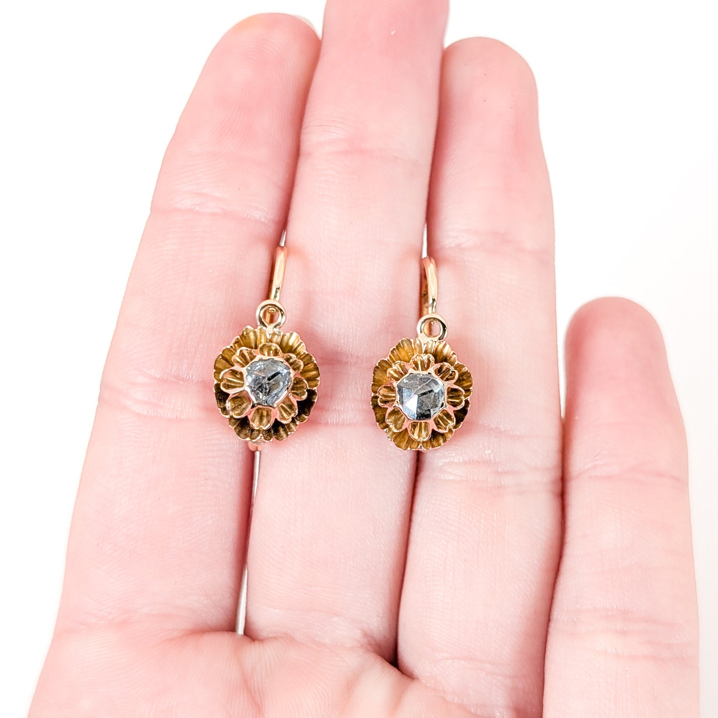 Antique Gold floral earrings with a central rose cut diamond gemstone held in a hand on a white background