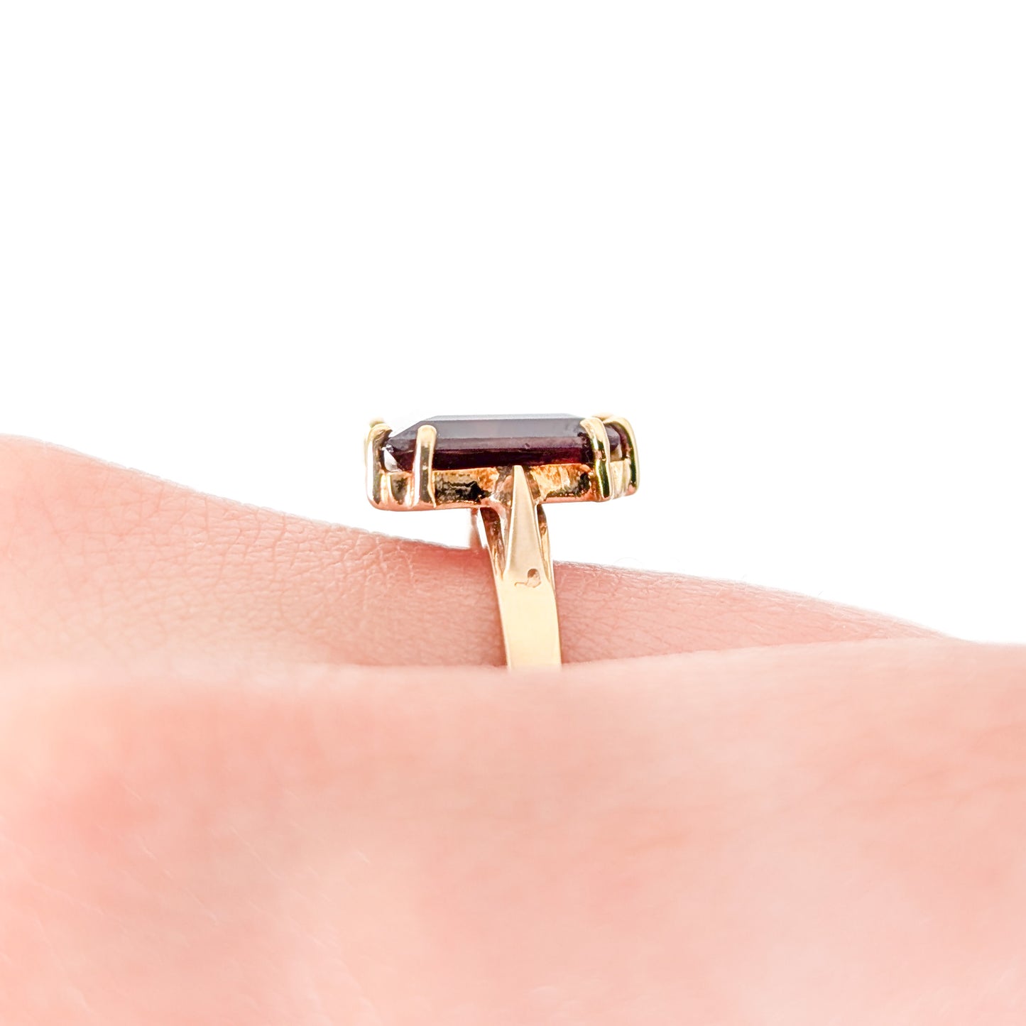 14K Gold garnet ring, cut into a striking trapezoid shape on a hand on a finger against a white background