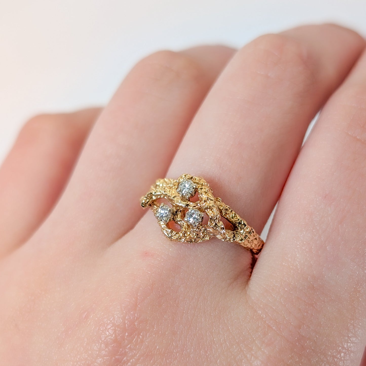 Gold ring with diamonds on a finger against a white background