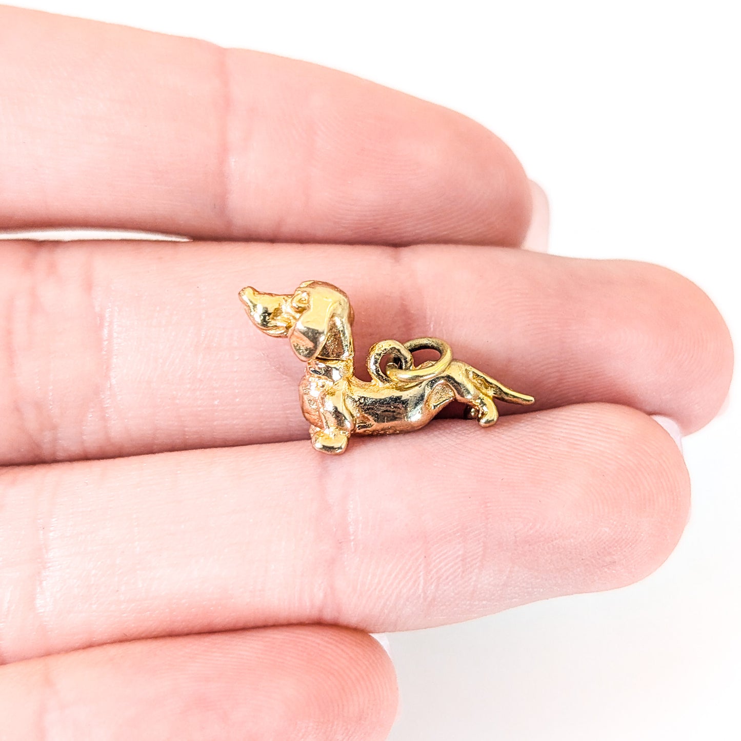 14K Gold dachshund mechanical charm held between fingers on a white background