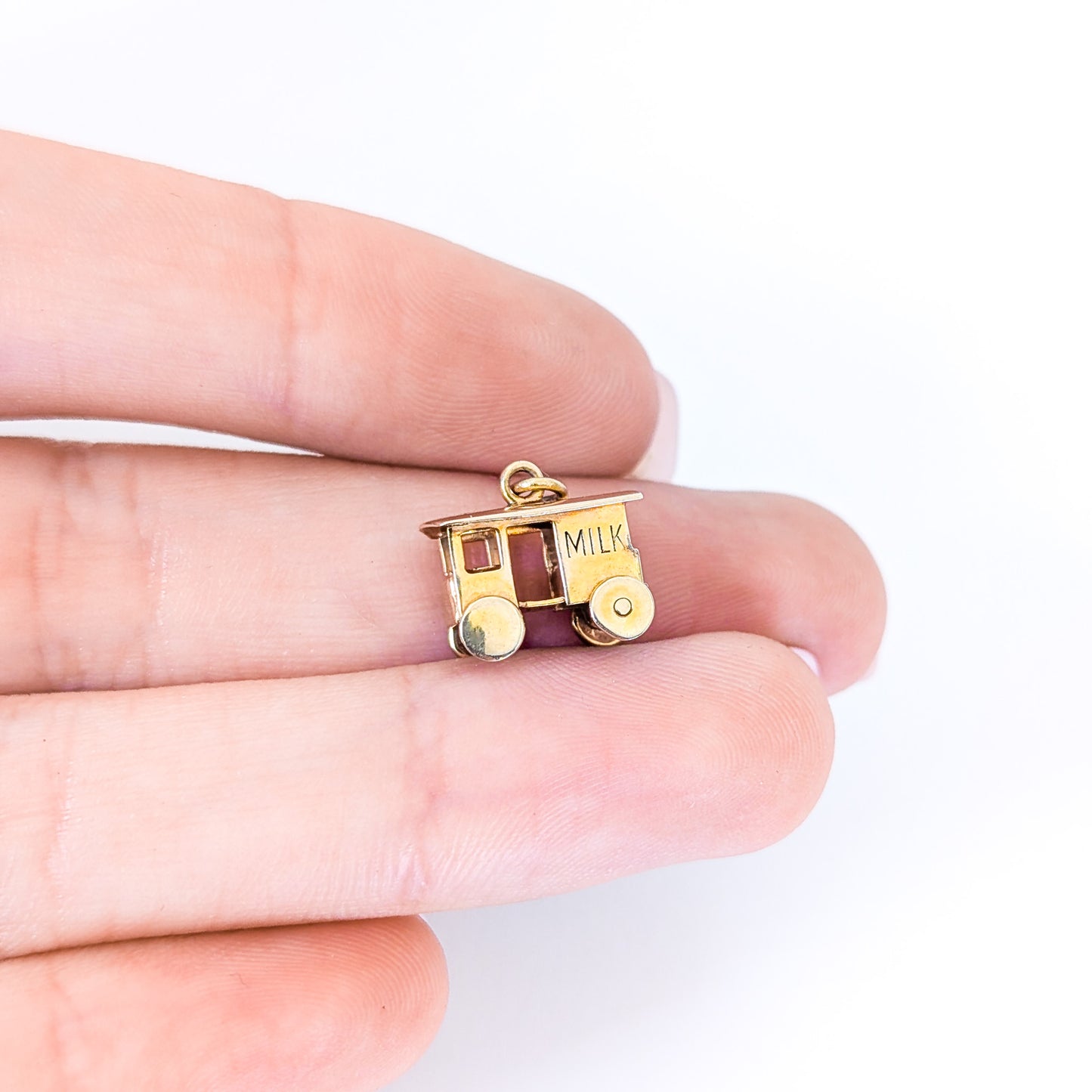 14K Gold milk cart mechanical charm held between fingers on a white background