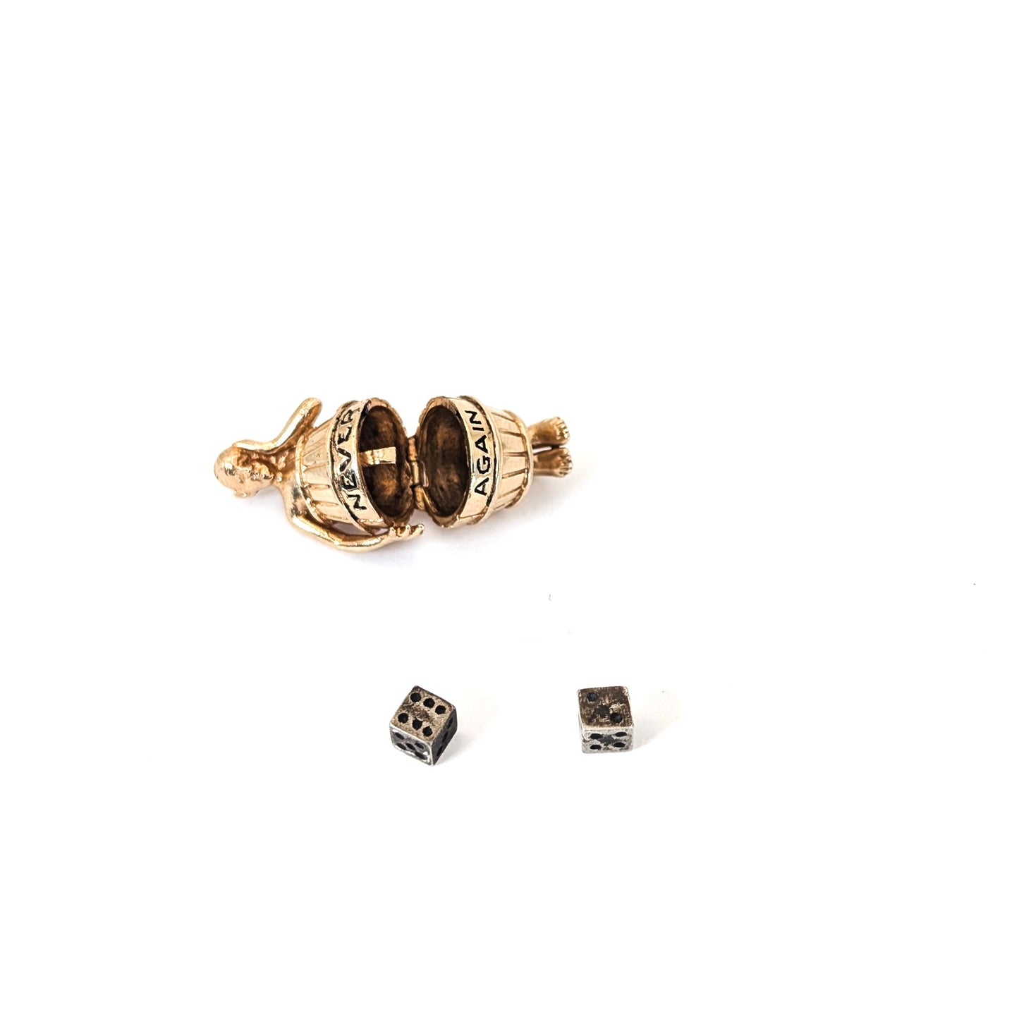 14K gold mechanical cram of a man in a barrel with 'Never Again' engraving and two small silver dice on a white background