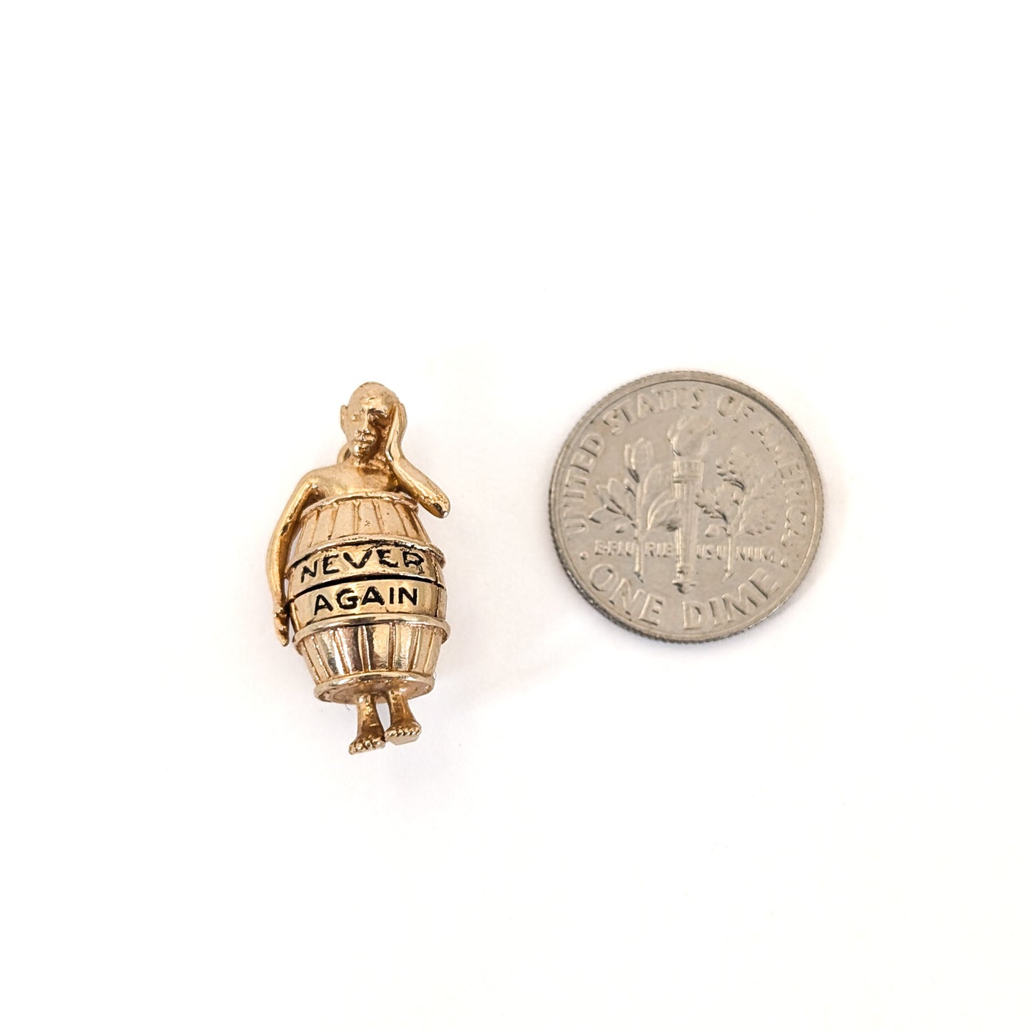 14K gold mechanical cram of a man in a barrel with 'Never Again' engraving next to a coin on a white background