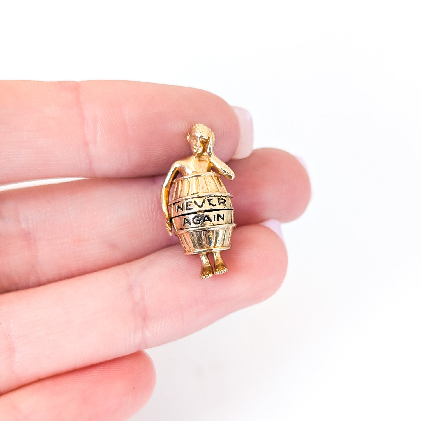 14K gold mechanical cram of a man in a barrel with 'Never Again' engraving held between fingers on a white background