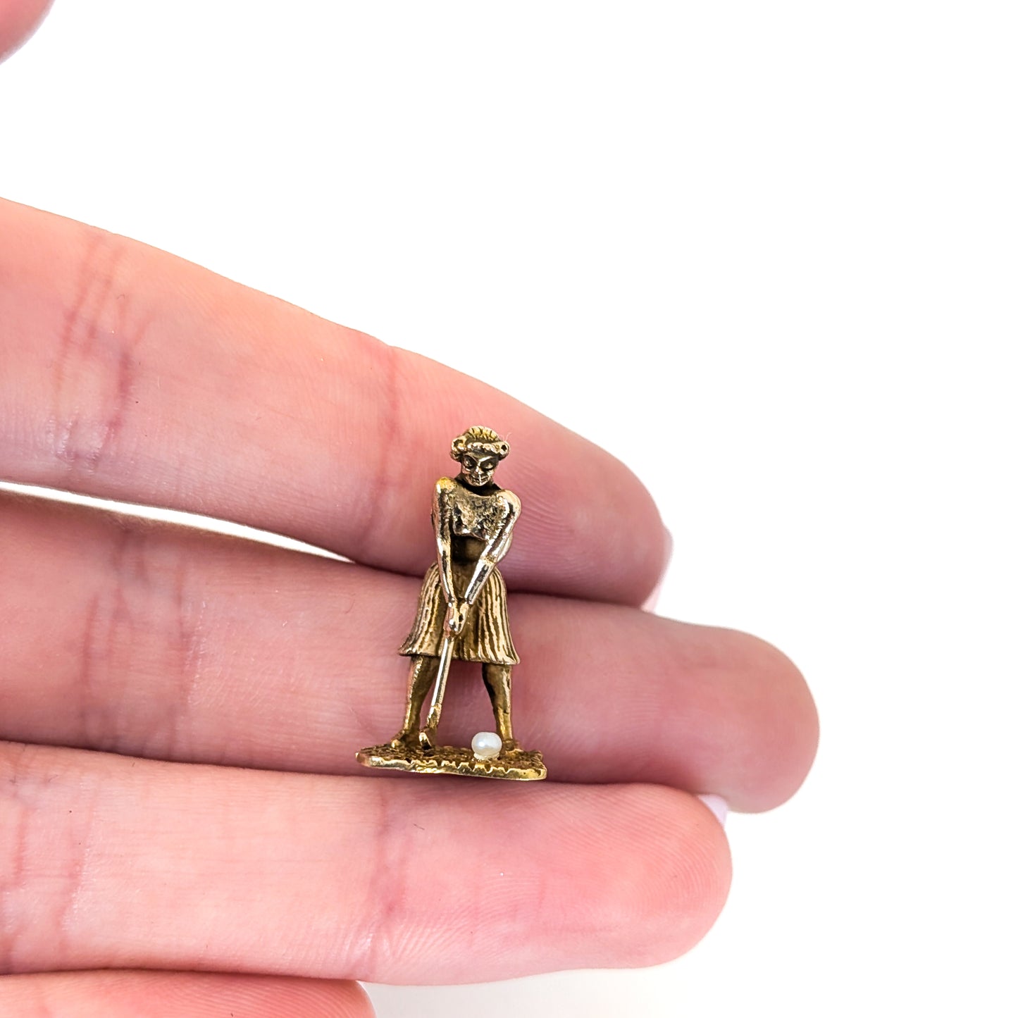 14k Gold vintage mechanical charm of lady playing golf with a pearl golf ball held between fingers on a white background