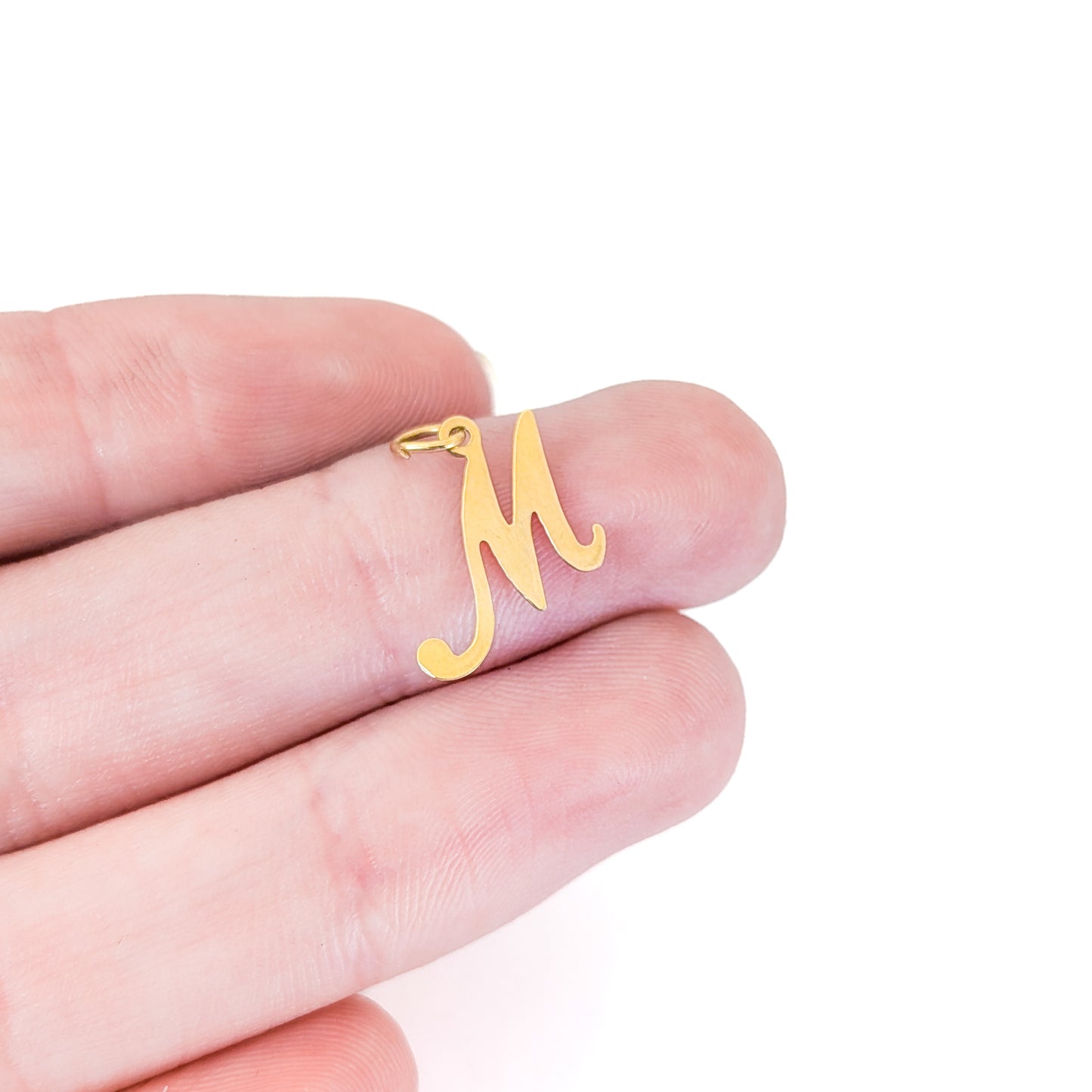 14K Gold letter 'M' pendant held between fingers on a white background