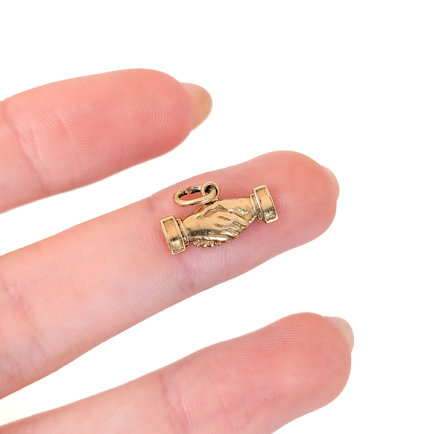 14k Gold handshake charm on a finger against a white background