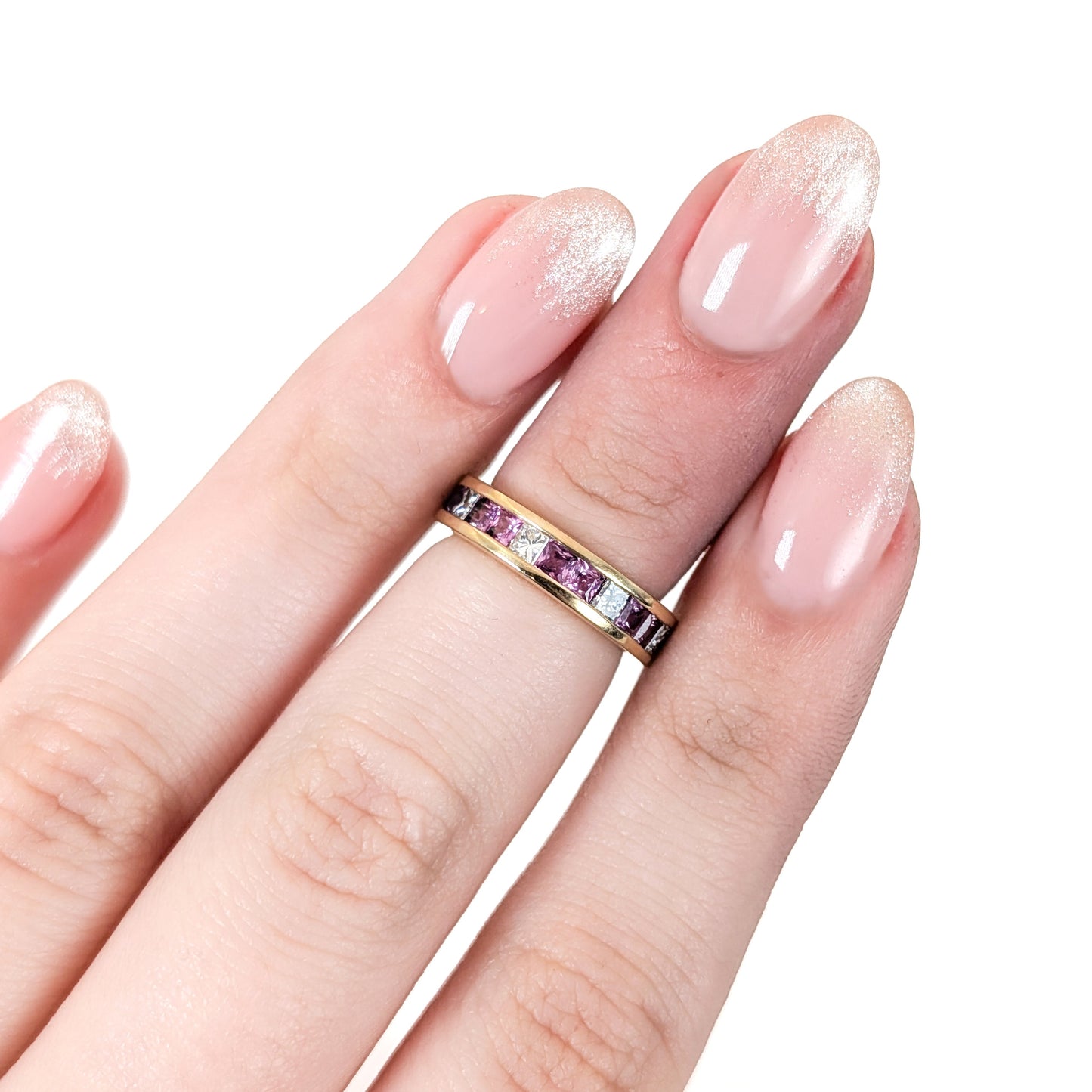 Hand wearing 14k gold eternity band with pink sapphires and diamonds on a white background
