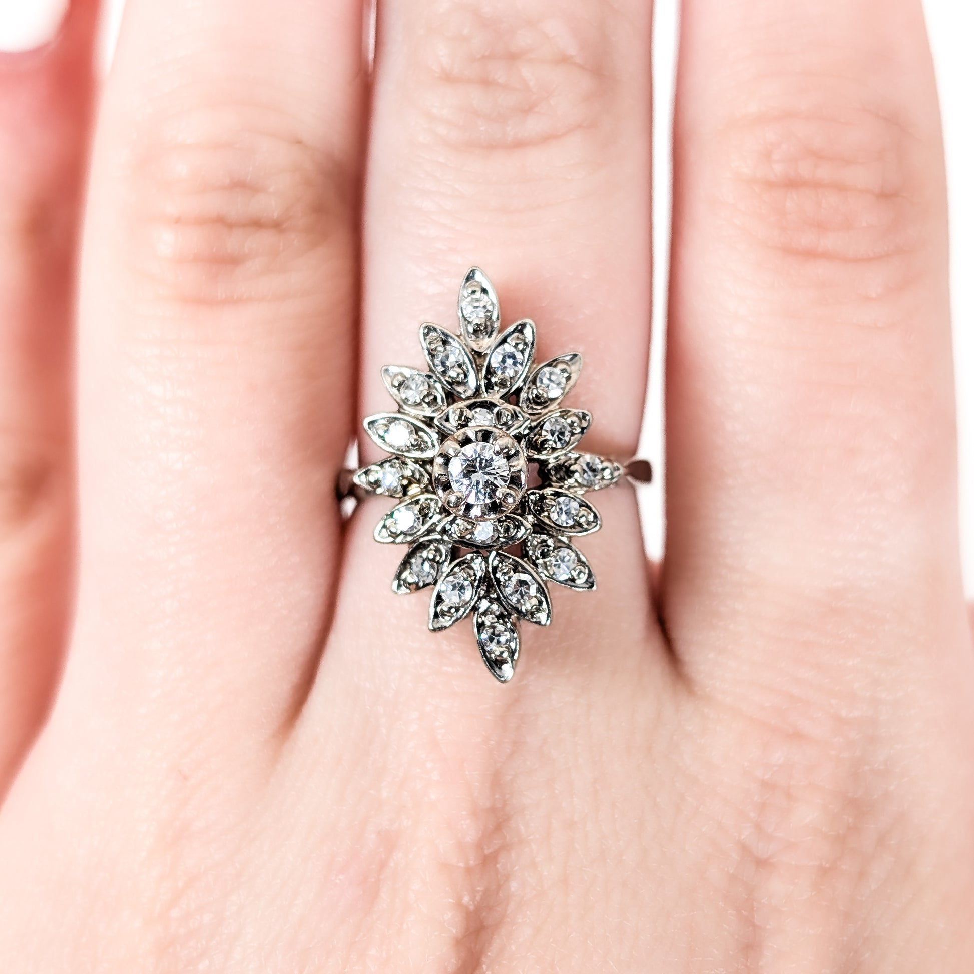 Luminous 14K white gold ring , the design features a brilliant round center diamond surrounded by an intricate halo of marquise-shaped with round diamond accents on a finger on a hand