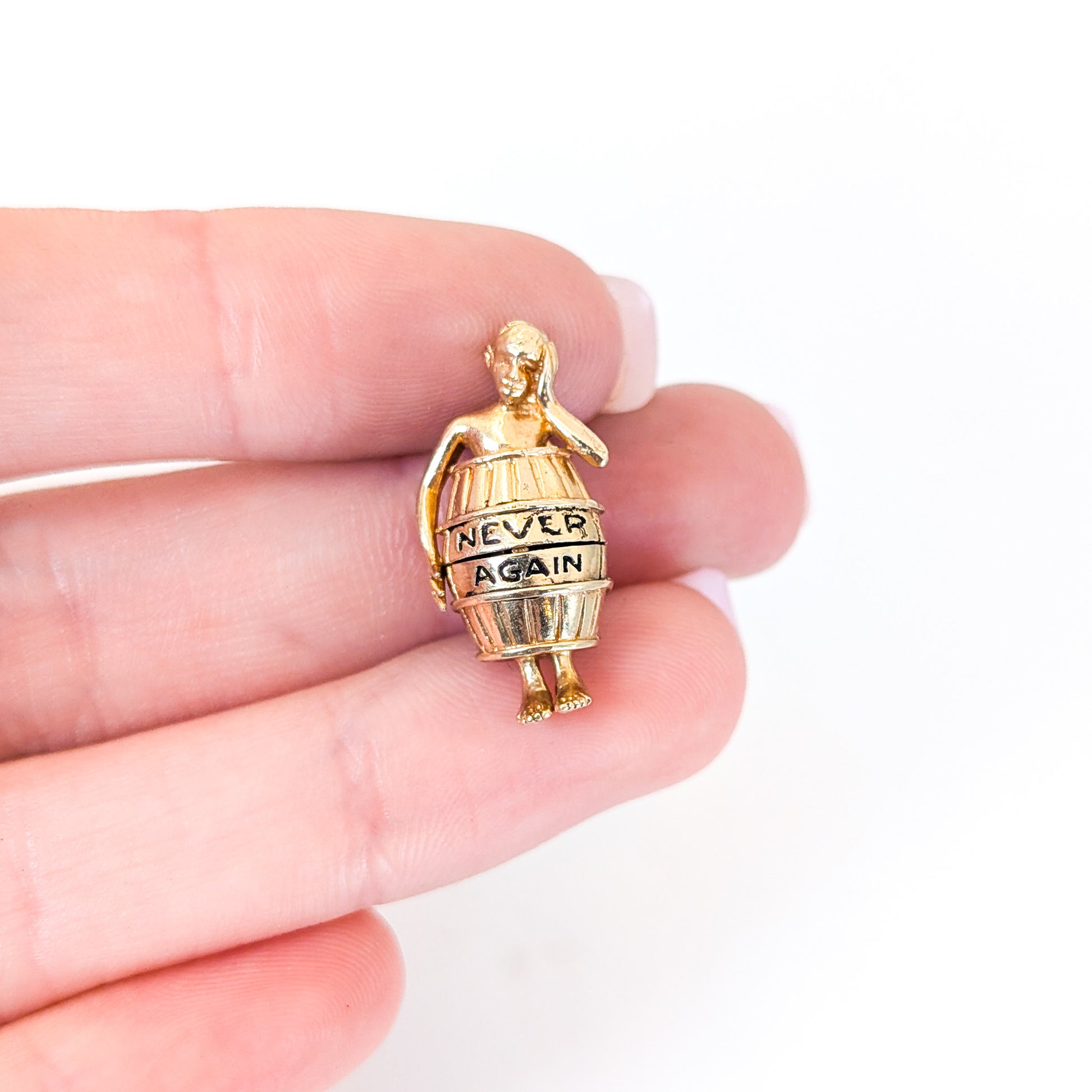 14K gold mechanical cram of a man in a barrel with 'Never Again' engraving  held between fingers on a white background