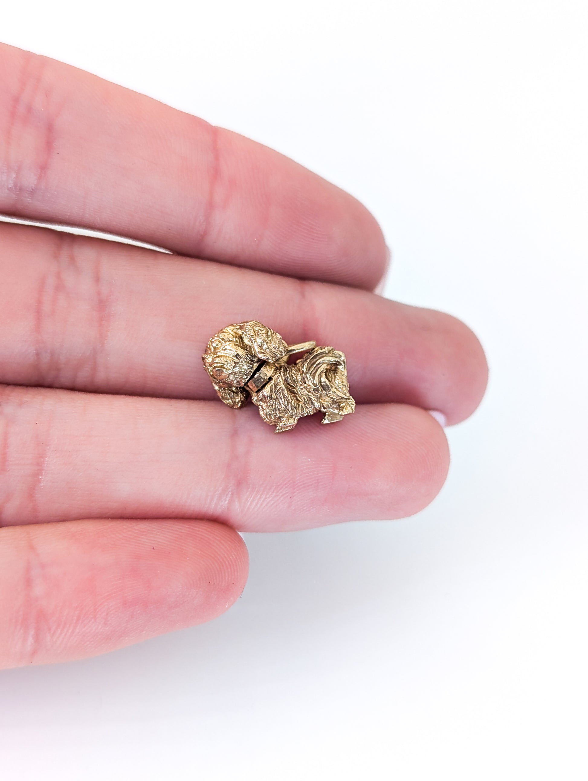14k Gold Vintage Pekingese mechanical charm held between fingers on a white background
